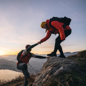 Young woman offers man a hand up, in the Swiss Alps